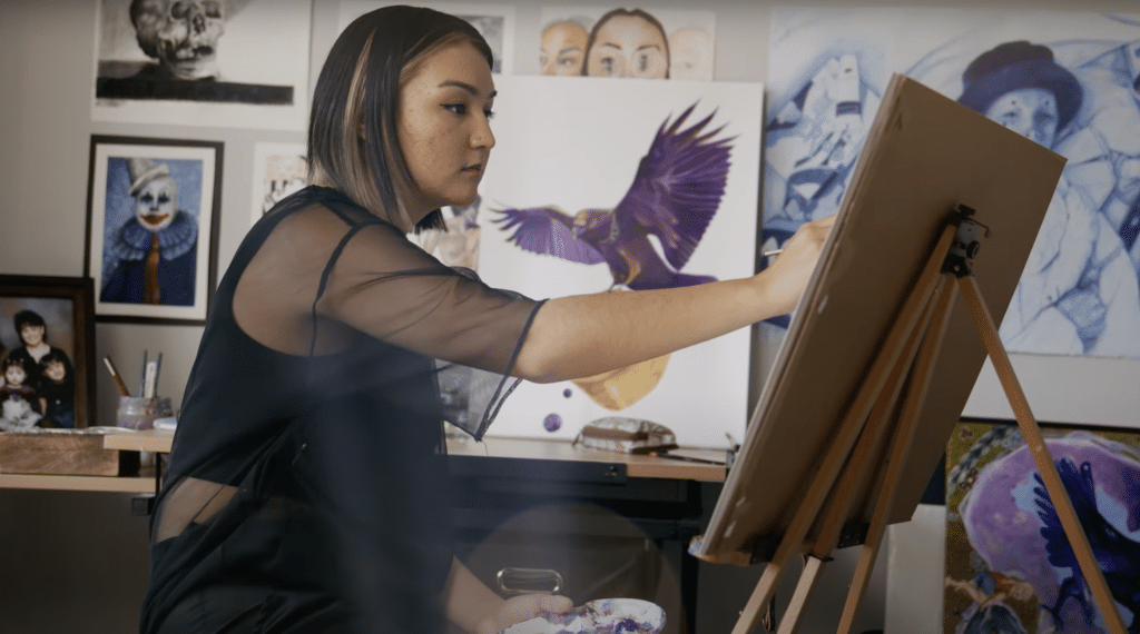 A woman paints on an easel surrounded by art